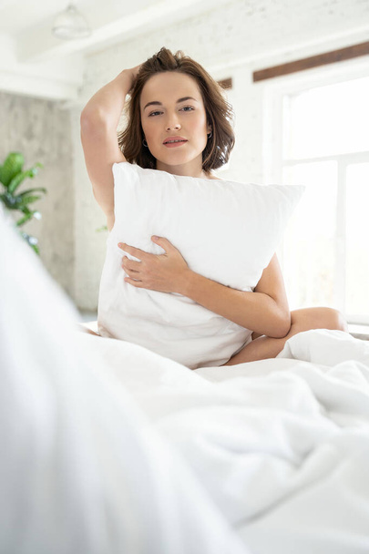Mujer tranquila sosteniendo una almohada en la cama
 - Foto, imagen