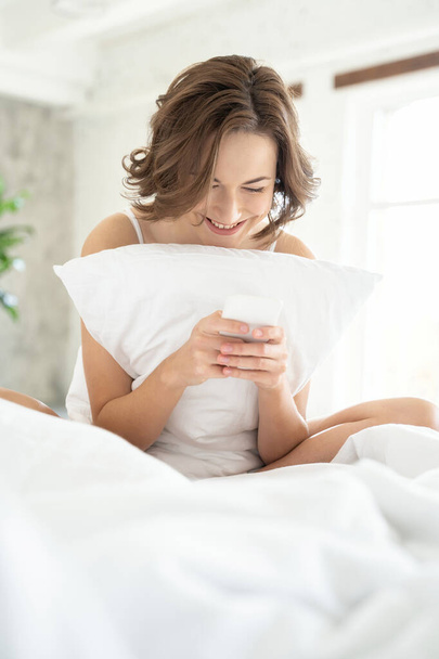 Atractivo feliz joven dama mensajes de texto en la cama
 - Foto, imagen