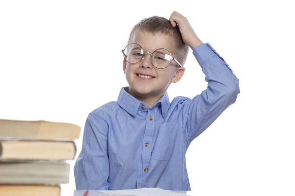 Een schooljongen met een bril zit aan een tafel en lacht. Geïsoleerd over witte achtergrond. - Foto, afbeelding