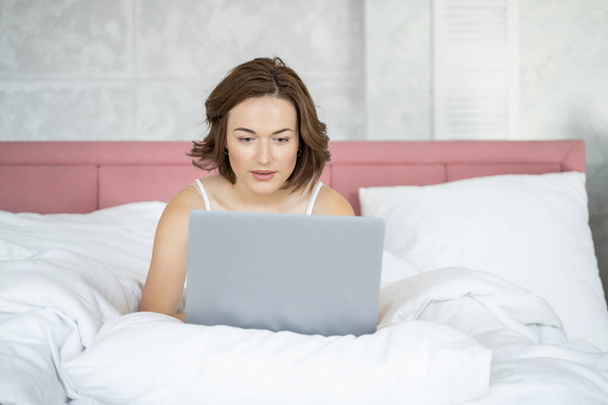 Pretty woman working on her laptop in bed - Photo, Image