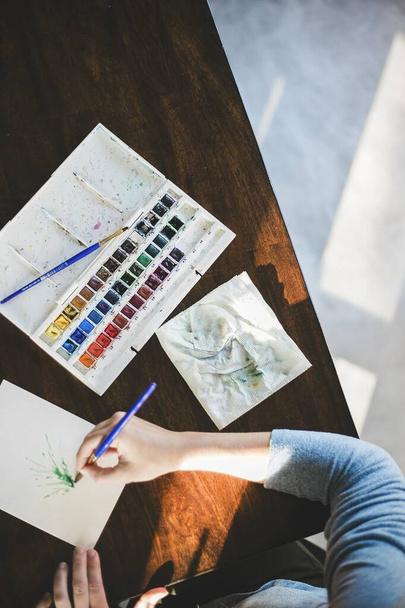Overhead shot of a person painting with watercolors and a white watercolor palette. - Photo, Image