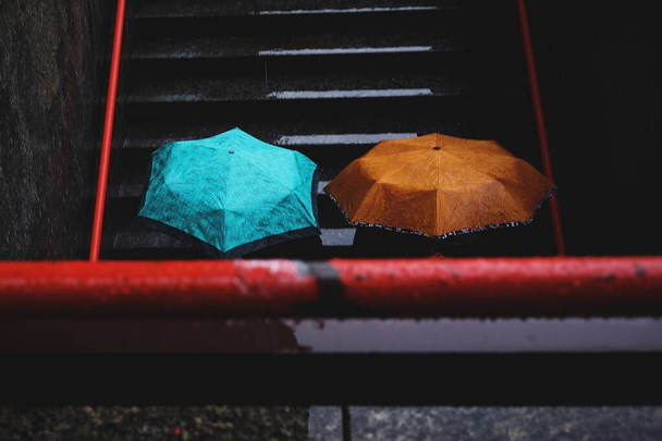 Horizontal shot of two persons going down the stairs while holding a cyan and brown umbrellas - Foto, Imagem