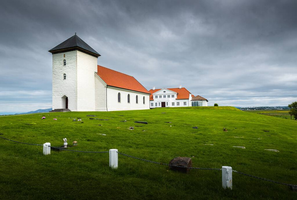 Simple white church and tower sit in plain grounds before a large grand residence in Iceland - Fotó, kép