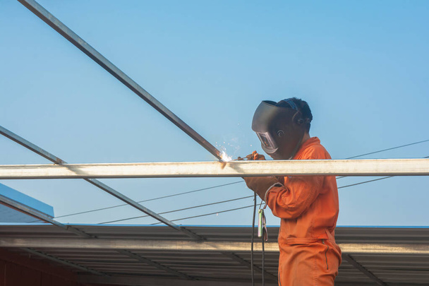 Soudage des travailleurs dans les vêtements de travail orange Soudage Pour treillis de toit
 - Photo, image