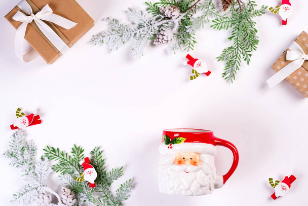 Уютная рождественская концепция. Рождественские игрушки, зеленые елки, чашка Санта Клауса и подарочная коробка на белом столе. Плоское пространство для копирования
 - Фото, изображение