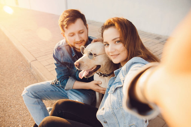 Щаслива красива пара розважається з лабрадором собакою-ретривером на відкритому повітрі роблячи селфі фото
 - Фото, зображення
