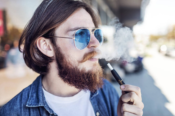 ひげを生やした若い喫煙者電子タバコ屋外 - 写真・画像