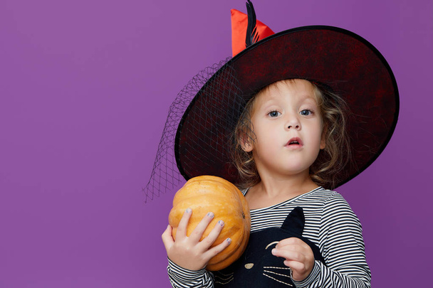 Fijne Halloween! Schattig geschokt klein kind meisje in heks kostuum en hoed op violette of paarse achtergrond.  - Foto, afbeelding