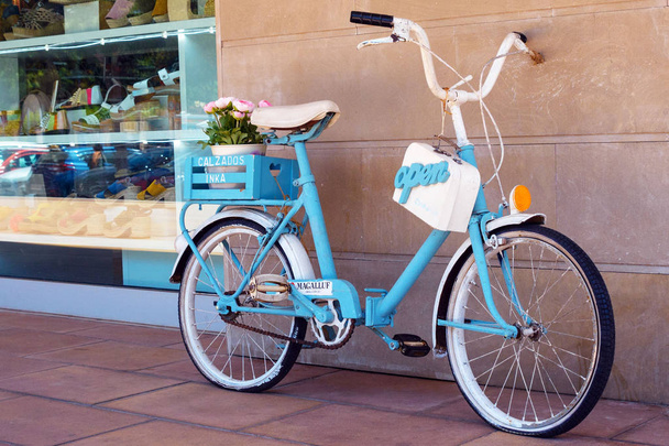 Maiorca, Spagna, luglio 2019. Vecchia bicicletta retrò blu con fiori in un cesto vicino al negozio. Disposizione decorativa elegante del negozio
. - Foto, immagini