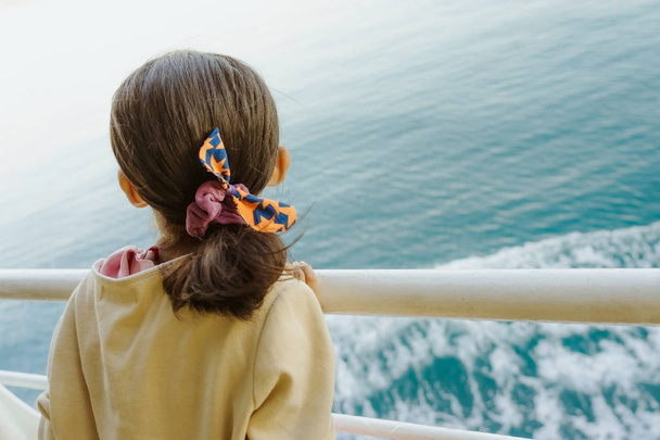 Азійська дівчинка стоїть на балюжі порому, щоб розслабитися і подивитися на океан і острів. - Фото, зображення