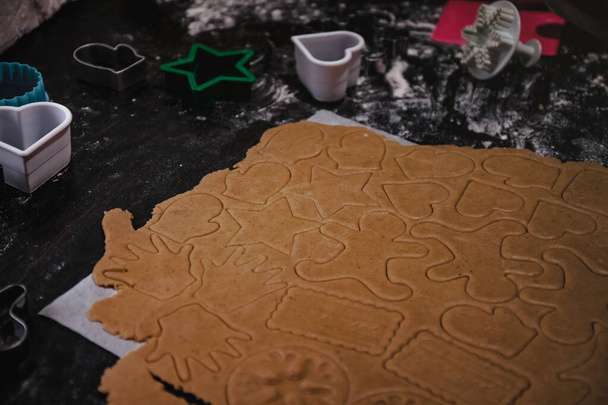 cut out gingerbread cookie in the form of a Christmas tree, star, little man, hearts from raw dough on parchment baking paper on a dark background. Top view. save space - Photo, Image