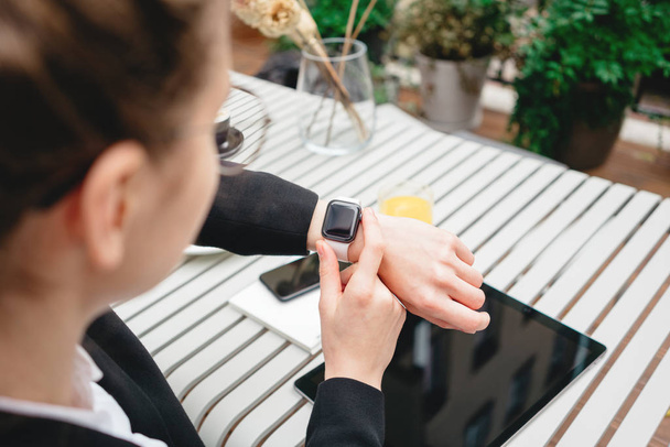Top view of businesswoman using smartphone and smartwatch for conversation with customers digital social media project. Business lady sitting on veranda in coffee shop and using modern gadgets - Фото, зображення