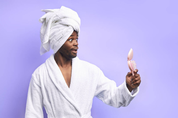 fröhlicher afrikanischer Mann in Bademantel und Handtuch mit Blick auf rosa Spiegel - Foto, Bild