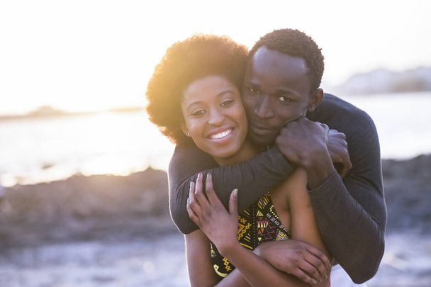 ευτυχισμένο ζευγάρι Αφρικάνων ερωτευμένων ή φίλων μένουν μαζί αγκαλιασμένοι με μεγάλα χαμόγελα στο φως του ήλιου του καλοκαιριού  - Φωτογραφία, εικόνα
