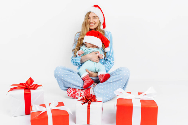 A young mother, on Christmas day gives a gift to a newborn child, a girl holds a baby in her arms with a Christmas gift - Photo, Image