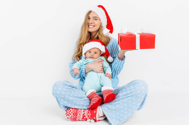 A young mother, on Christmas day gives a gift to a newborn child, a girl holds a baby in her arms with a Christmas gift - Foto, Imagem
