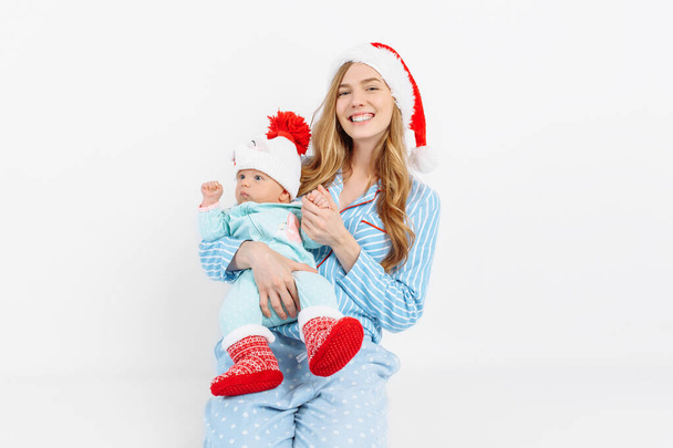 A young mother, on Christmas day gives a gift to a newborn child, a girl holds a baby in her arms in a Christmas hat - Foto, Bild