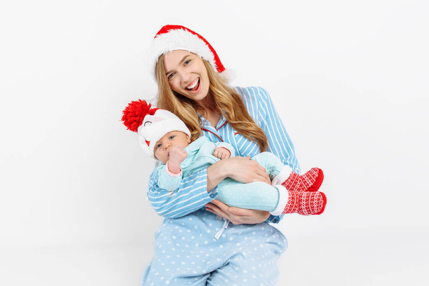 A young mother, on Christmas day gives a gift to a newborn child, a girl holds a baby in her arms in a Christmas hat - Foto, afbeelding