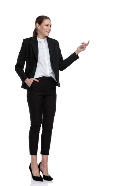 mujer de negocios de pie con la mano en el bolsillo y señalando a un lado
 - Foto, imagen