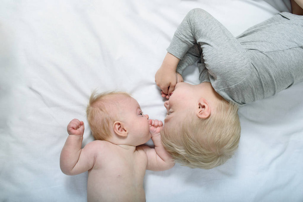 Baby and smiling older brother are lying on the bed. Funny and interact. Top view - Foto, immagini