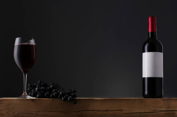 Μπουκάλι κόκκινο κρασί με ετικέτα και ποτήρι κρασιού σε παλιό ξύλινο τραπέζι - Φωτογραφία, εικόνα
