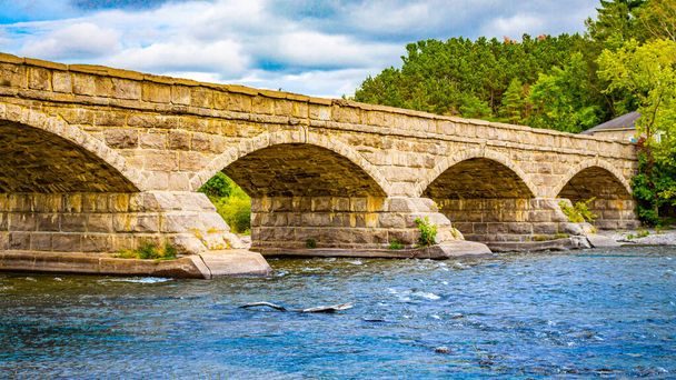 Ponte de pedra arqueada sobre um rio
 - Foto, Imagem