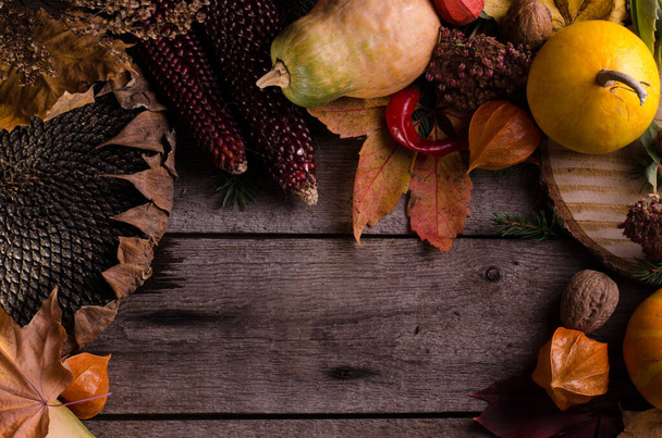 Sötét hangulatú vidéki csendélet élénk narancssárga sütőtökkel, napraforgóval, fizállal és színes őszi levelekkel. Őszi kompozíció egy régi fa felületen. - Fotó, kép