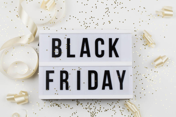 Black friday sale text on white lightbox, golden stars and holiday ribbon around on white background - Фото, зображення