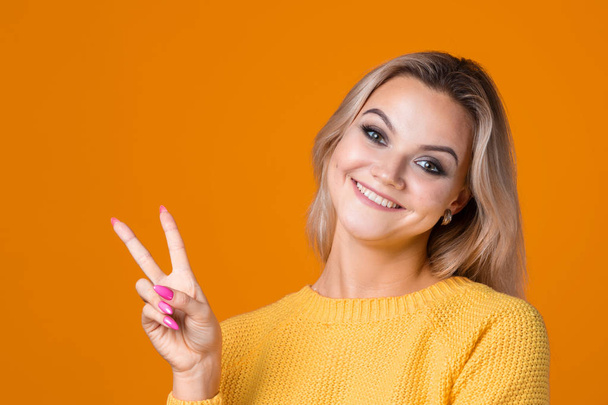 Happy and smiling blonde in a yellow sweater on a yellow background. - Foto, afbeelding