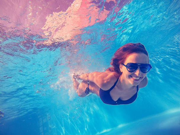 Πισίνα. Μια γυναίκα κολυμπάει στην πισίνα με γυαλιά ηλίου.. - Φωτογραφία, εικόνα