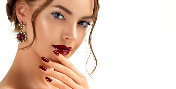Beautiful model girl with burgundy or wine color manicure on nails . Fashion makeup and cosmetics . Jewelry, earrings and accessories. Beauty woman with braid hairstyle around her head. - Photo, Image