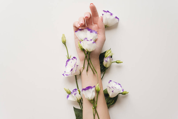 The hand and spring flowers of eustoma are on a white table. the concept of skin care. Natural cosmetics for hand skin care, a means to reduce wrinkles on the hands, moisturizing. Natural flower extra - Foto, Imagen