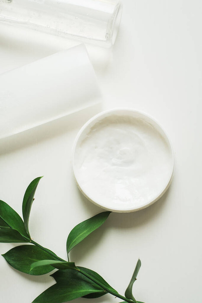 Means for skin care, rejuvenation and hydration of the face. Cream, micellar water and moisturizing lotion on a white background with a branch of green . The philosophy of self care and skin care - Fotó, kép