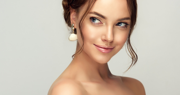 Beautiful woman with clean skin on her face. Girl model with braided braid around her head. Hairstyle in the trend. Beauty, cosmetics and cosmetology. Fashion earrings as accessories - Photo, Image
