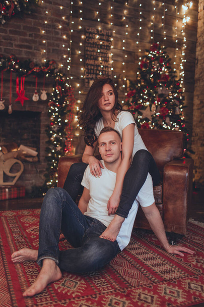Lovely beautiful couple woman and man are sitting at home near fireplace. Christmas time. - Φωτογραφία, εικόνα