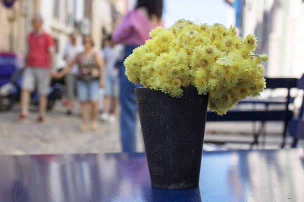 chrysanthemums yellow blossom stands in black pot on table. People walking in the background - Photo, Image