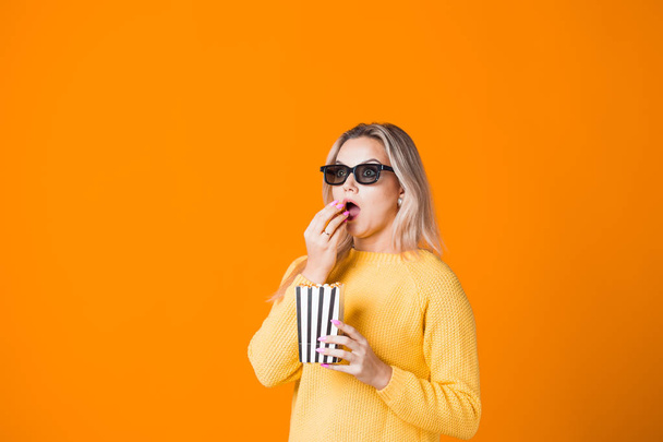 Young cheerful woman in 3D glasses watching a movie and eating popcorn. - Photo, Image