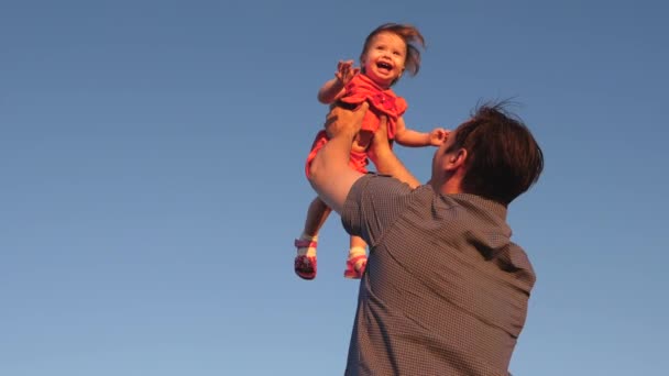 Батько кидає дитину на блакитне небо, тато грає з маленькою донькою, дитина посміхається і радіє. Повільний рух. щаслива сім'я грає ввечері проти неба
. - Кадри, відео