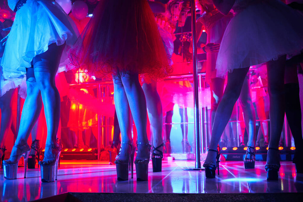 Jóvenes sexy womans pole bailando striptease en club nocturno. Hermosa chica stripper desnuda en el escenario. Hermosas piernas femeninas en tiras de zapatos de tacón alto
 - Foto, imagen