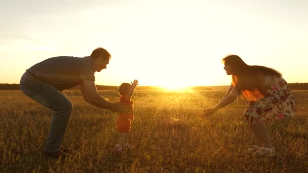 father and mother play on field with a little daughter in sun. little daughter goes from dad to mom in sun. mother, father and little daughter girl enjoying nature together, outdoors. Slow motion. - Footage, Video
