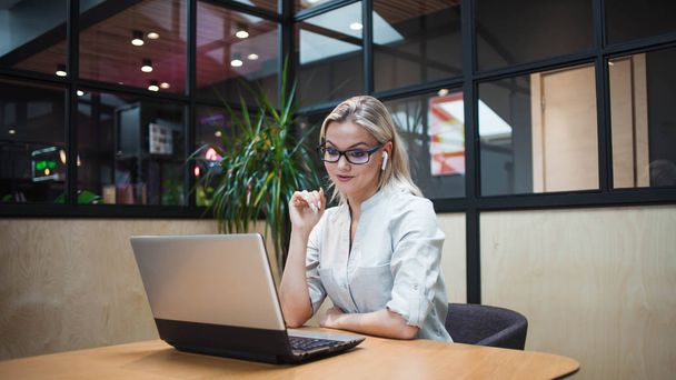 młoda kobieta w słuchawkach bezprzewodowych siedzi na laptopie i pracuje lub komunikuje się w sieci. - Zdjęcie, obraz