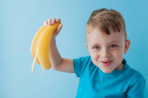 Little Boy Holding and eating an Banana on blue background, food - Фото, изображение