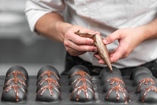 Making handmade chocolates. A confectioner pours liquid dark chocolate into molds. Close-up. - Foto, afbeelding