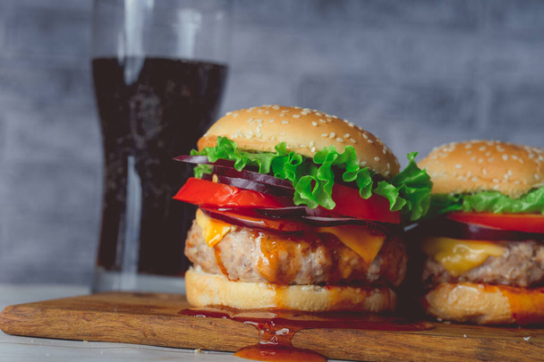 A two huge juicy hamburger is on a chopping board and large glass with cola - Foto, imagen