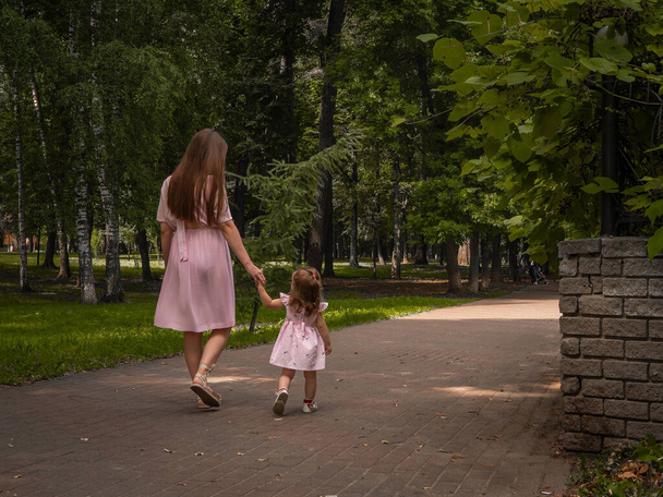 Mom and daughter walk and play in the park. Dressed in dresses. Sunny day, weekend in a city park. - Fotó, kép