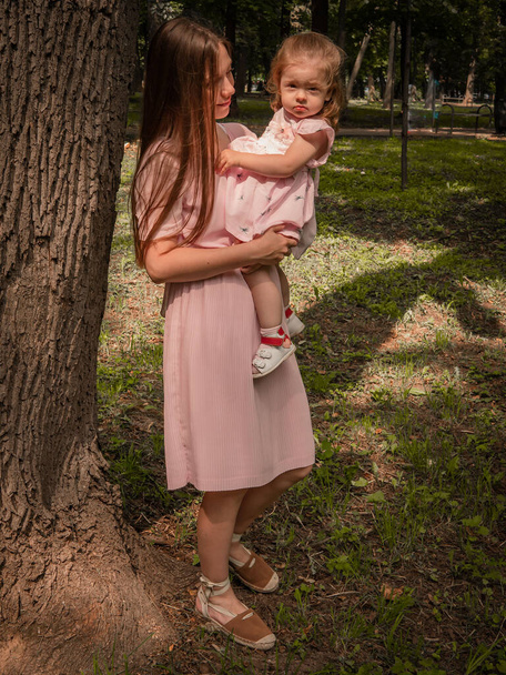 Mom and daughter walk and play in the park. Dressed in dresses. Sunny day, weekend in a city park. - Фото, изображение