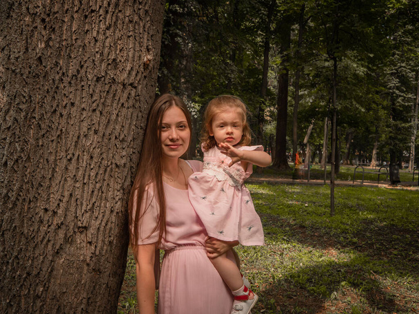 Mom and daughter walk and play in the park. Dressed in dresses. Sunny day, weekend in a city park. - Foto, Imagem