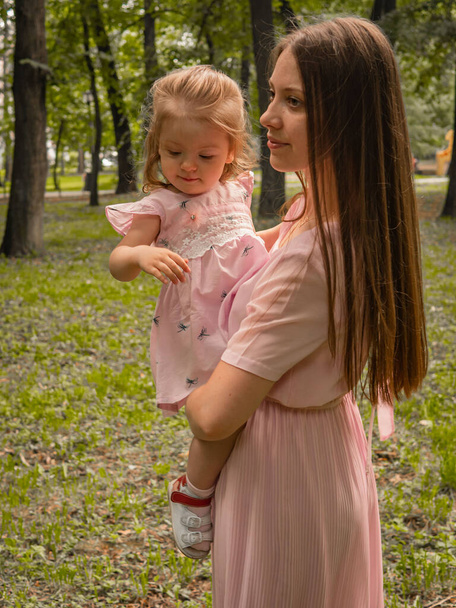 Mom and daughter walk and play in the park. Dressed in dresses. Sunny day, weekend in a city park. - Foto, Imagen
