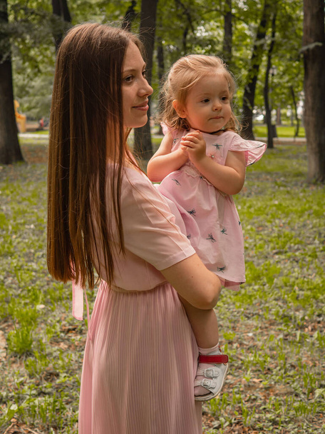 Mom and daughter walk and play in the park. Dressed in dresses. Sunny day, weekend in a city park. - Foto, afbeelding