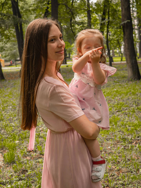 Mom and daughter walk and play in the park. Dressed in dresses. Sunny day, weekend in a city park. - Foto, afbeelding